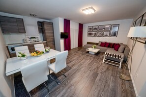 A modern living room with a sofa, a coffee table, and a dining area with a table and chairs. - Sunset Apartments (Vir)