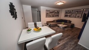 Un salon moderne avec un canapé, une table basse et un coin repas comprenant une table en verre et des chaises blanches.