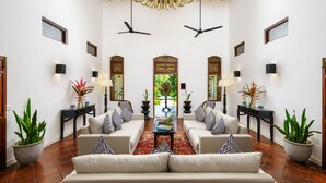 A spacious living area with a central sofa, two side tables with potted plants, a red patterned rug, and ceiling fans. - JH Villa (Unawatuna)