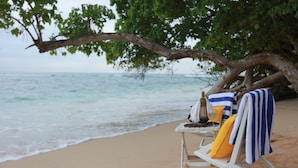 A beach chair with a towel and a bottle, positioned under a tree on a sandy beach. - JH Villa (Unawatuna)