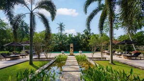 A pool area with lounge chairs, a stone pathway, and palm trees. - JH Villa (Unawatuna)