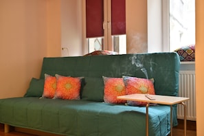 Ein grünes Sofa mit bunten Kissen, ein kleiner Tisch und ein Fenster mit Jalousien.