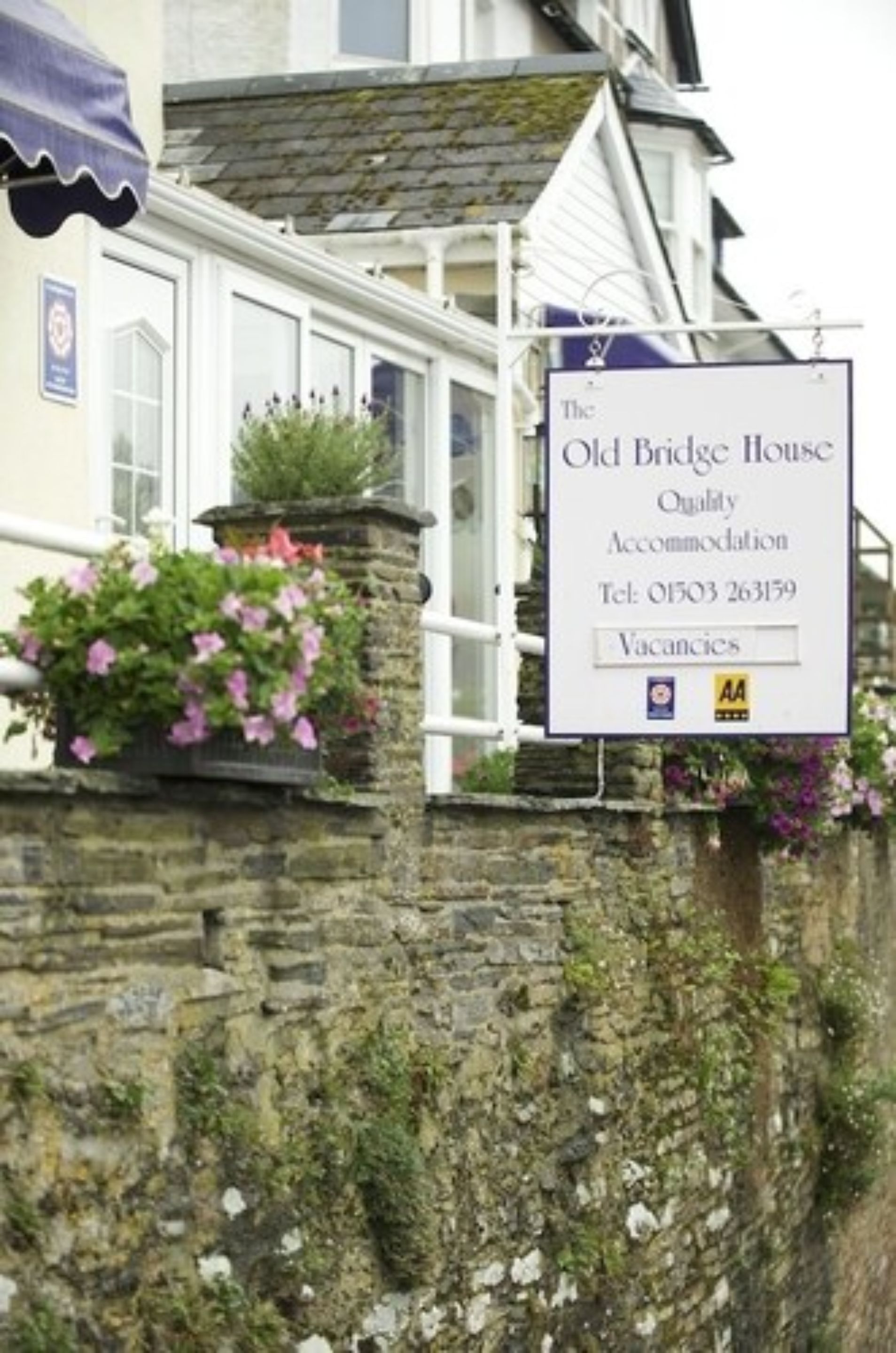 Señal de The Old Bridge House, que indica que es un alojamiento de calidad, con un número de teléfono y un aviso de habitaciones disponibles.
