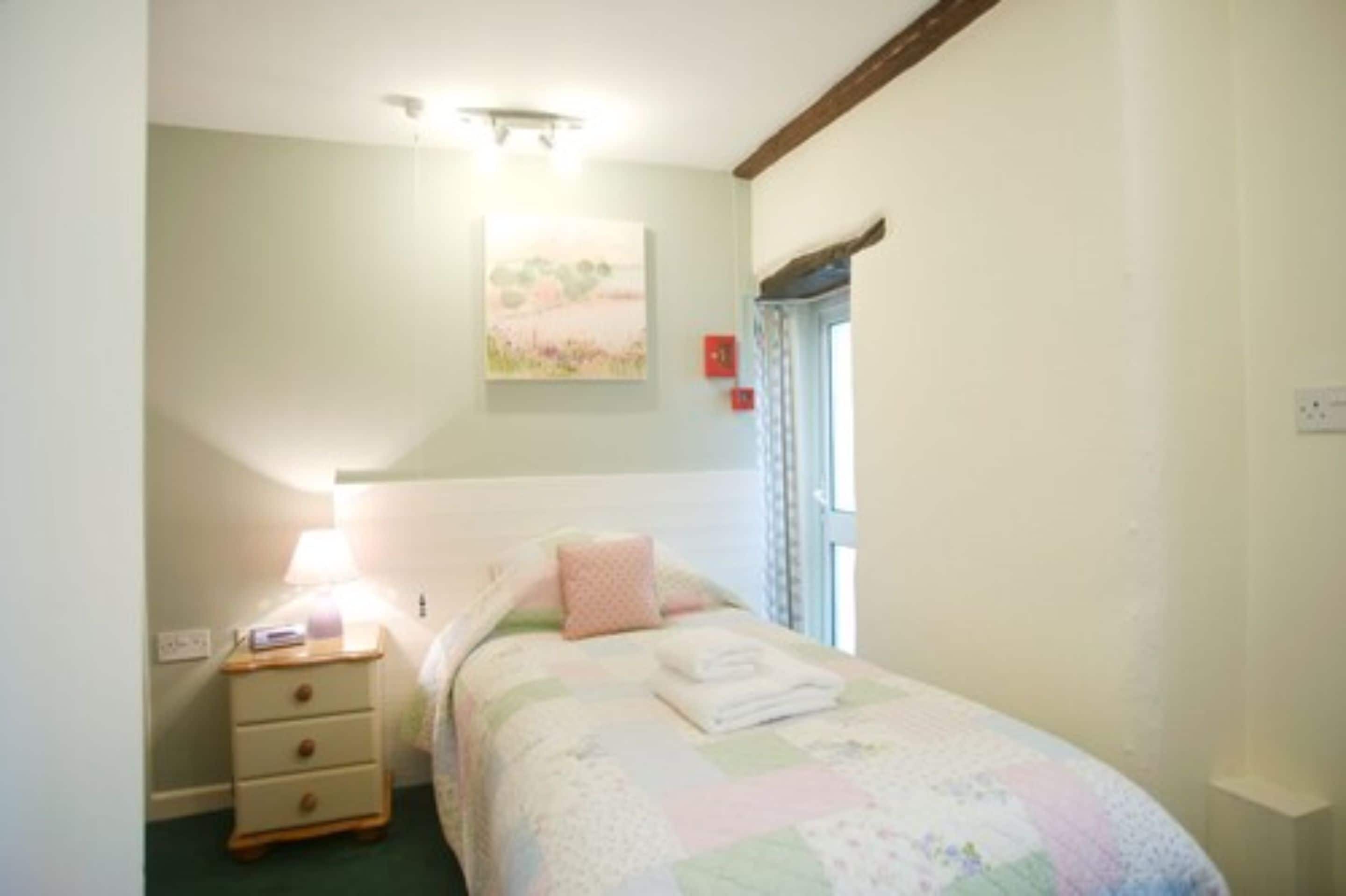 A bedroom with a bed, a nightstand, a lamp, and a painting on the wall.