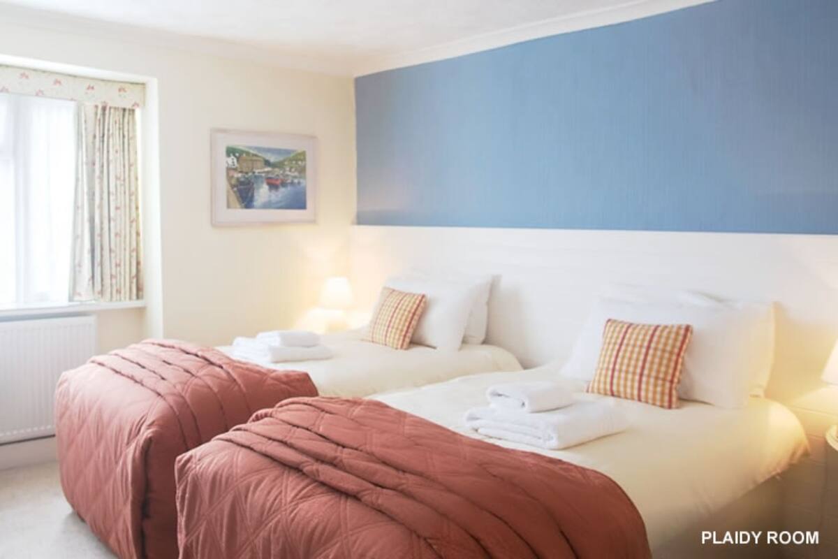 Habitación con dos camas, una silla y un ventanal con cortinas.