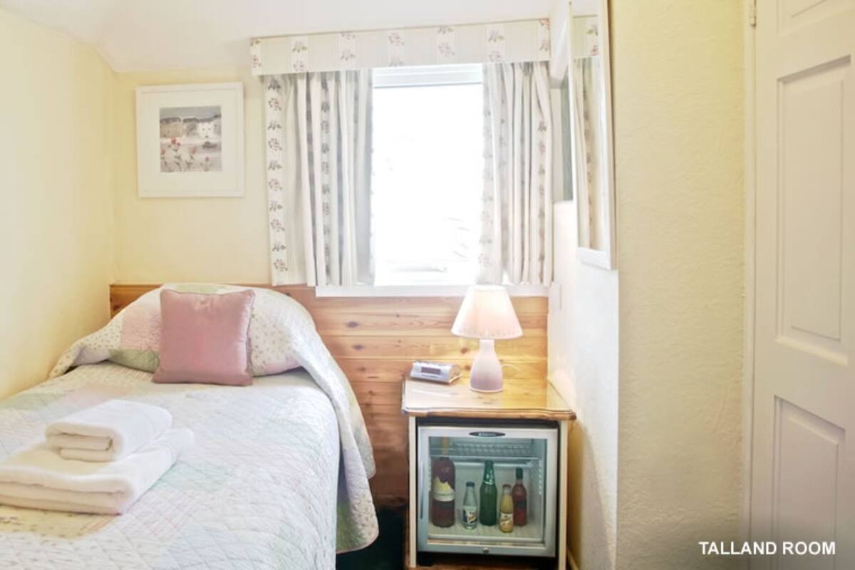 Un dormitorio con cama, una mesita de noche con lámpara, un refrigerador pequeño y una ventana con cortinas.