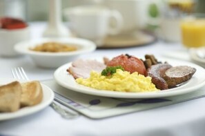 A breakfast plate with scrambled eggs, ham, sausage, and toast. - The Old Bridge House (Looe)