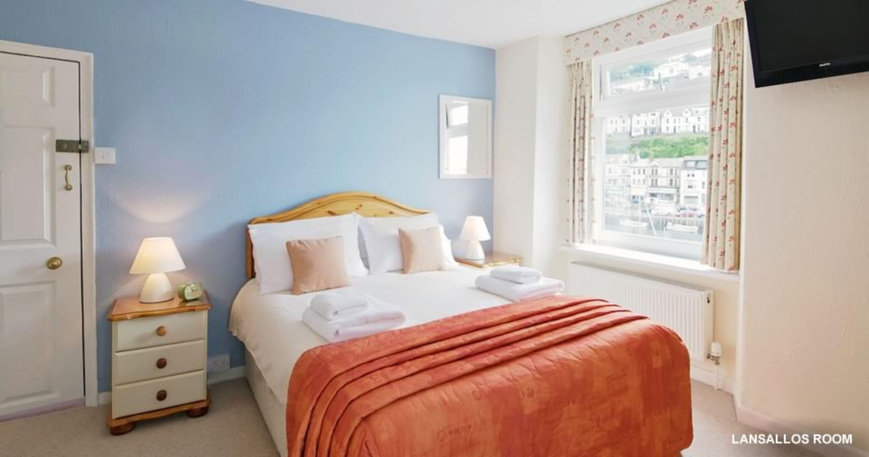 Una habitación de hotel con cama, lámparas de noche, ventana con vistas y puerta.