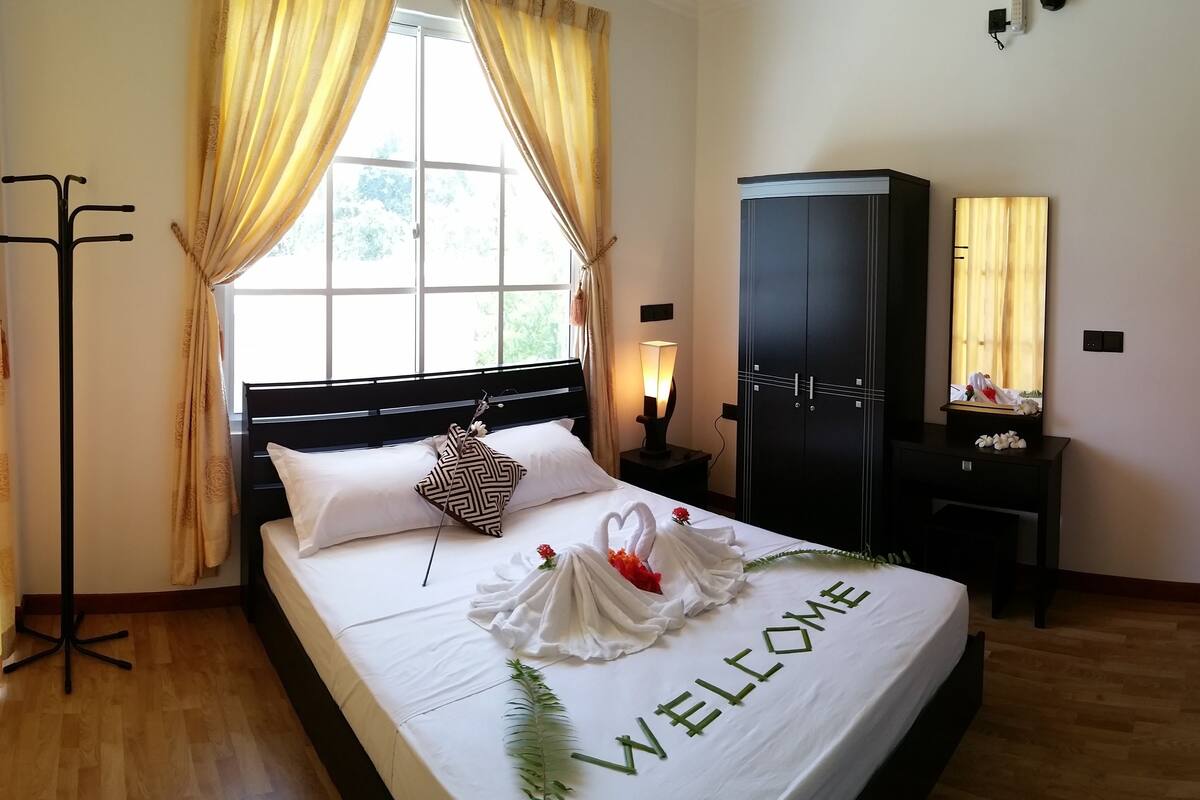 Una habitación de hotel con cama, armario, escritorio, televisor y ventana con cortinas.