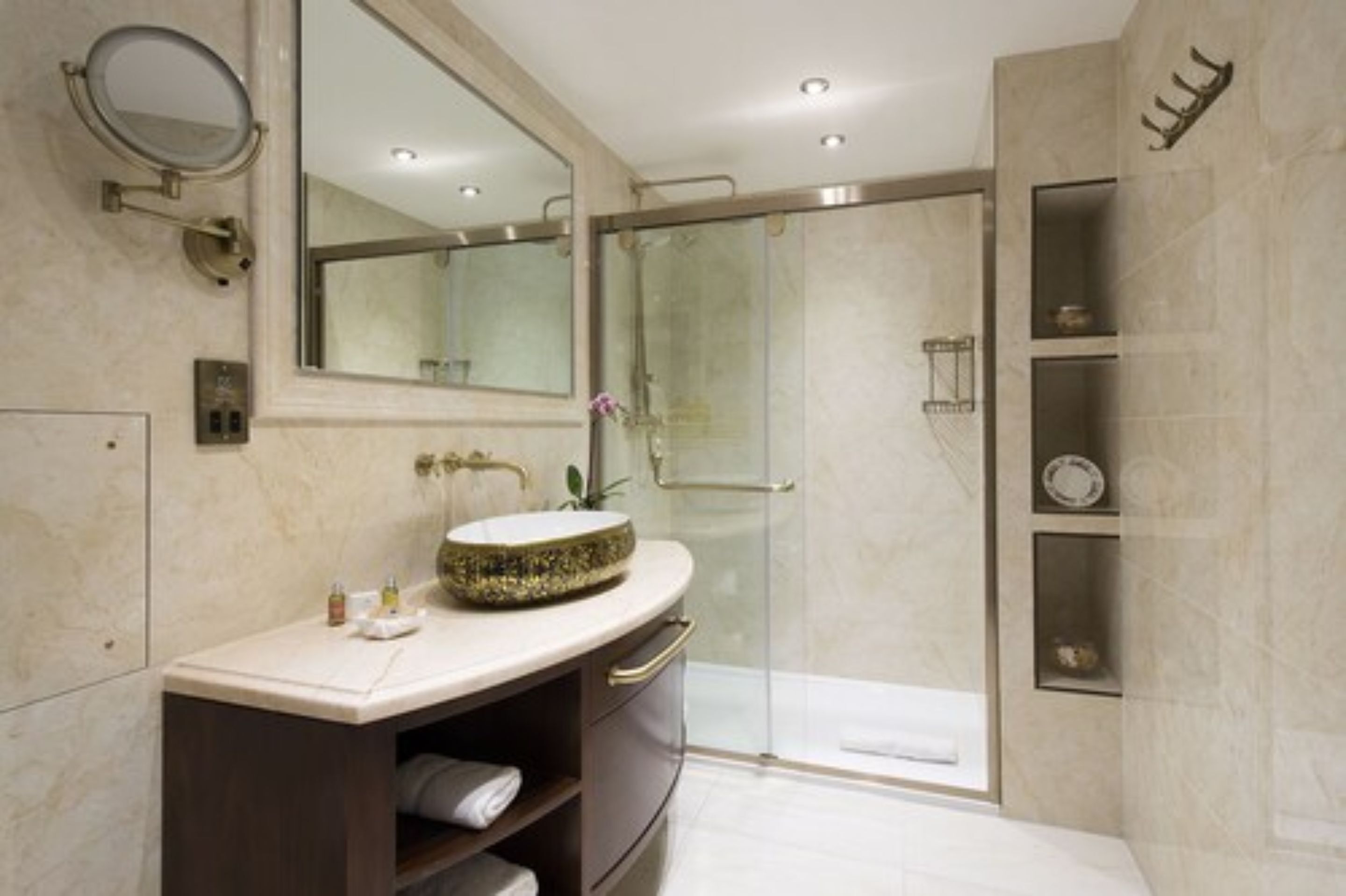 Une salle de bain moderne avec un grand miroir, un lavabo rond, une douche en verre et des murs en marbre.