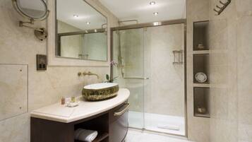 Un baño moderno con un espejo grande, un lavabo redondo, cabina de ducha de vidrio y paredes de mármol.