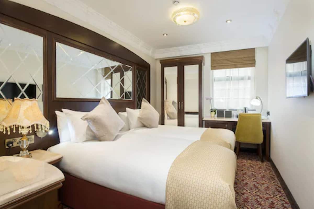 A hotel room with a large bed, a desk, a chair, and a mirror.