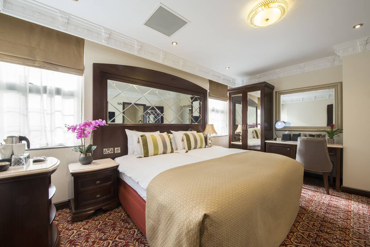 A hotel room with a large bed, a desk, a chair, a dresser, and a mirror.
