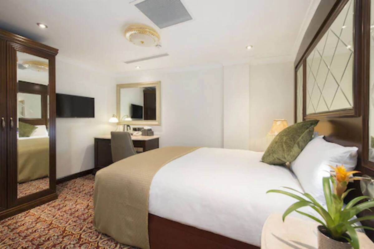 A hotel room with a large bed, a desk, a chair, a mirror, and a television.