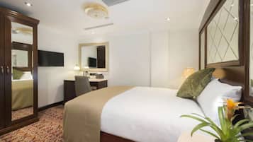 A hotel room with a large bed, a desk, a chair, a mirror, and a television.
