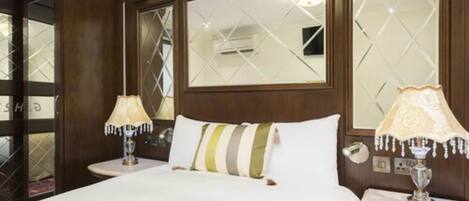 A hotel room with a large bed, two bedside tables with lamps, a mirror with a geometric pattern, and a wooden headboard.