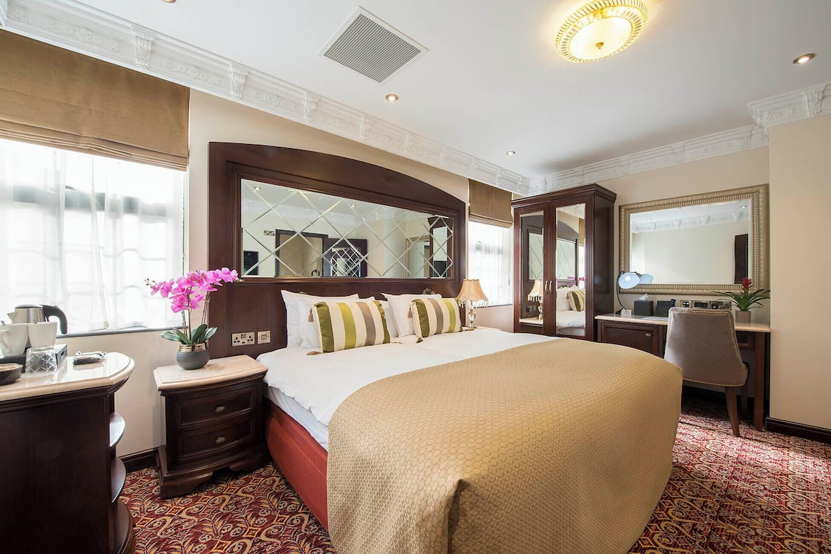 A hotel room with a large bed, a desk with a chair, a mirror, and a window with curtains.