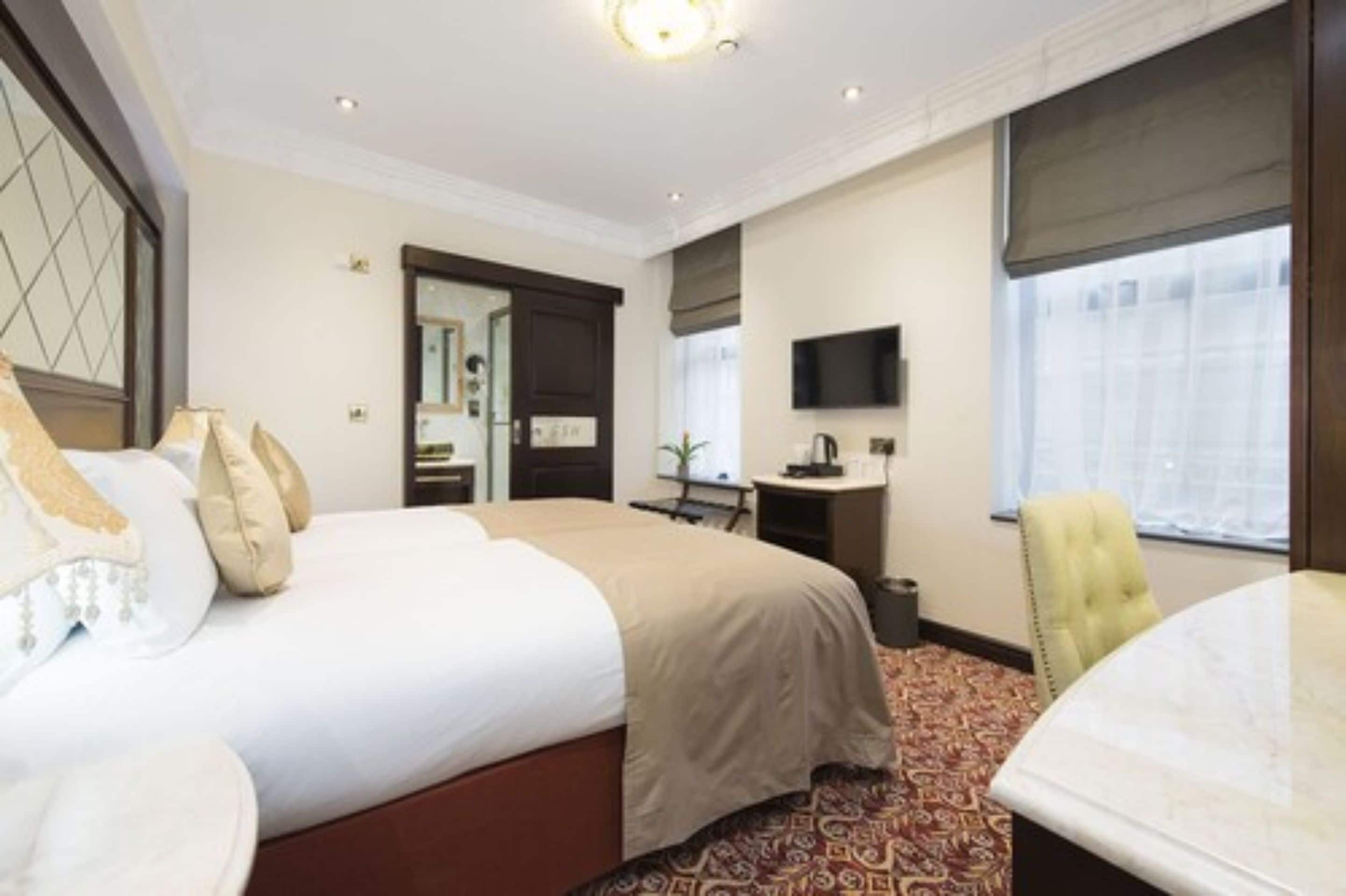A hotel room with a large bed, a desk, a chair, a television, and a window with curtains.