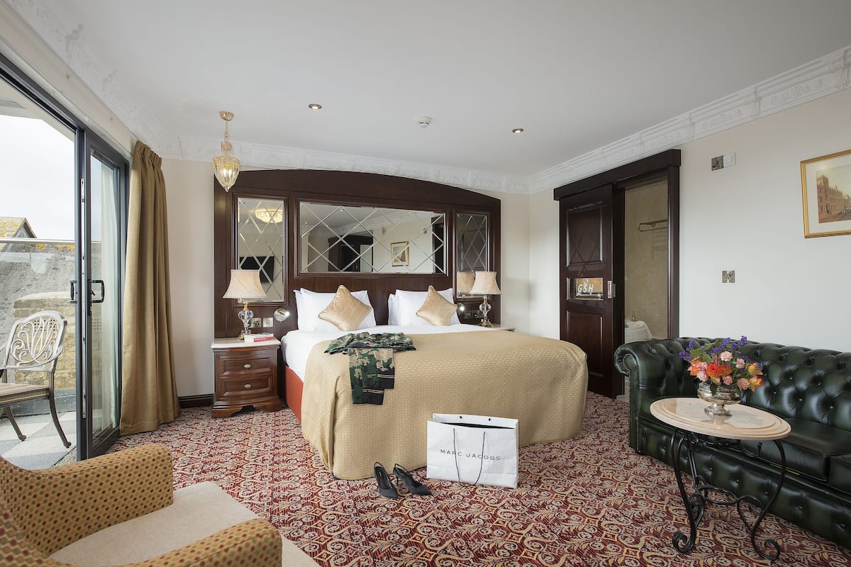 A hotel room with a large bed, a sitting area with a sofa, a small table, and a chair.