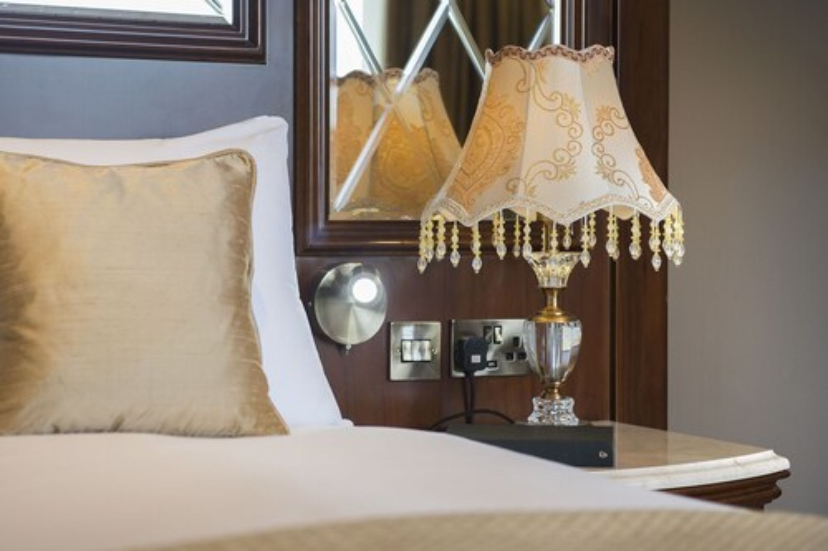 A neatly made bed with a gold-colored pillow and a decorative lamp with a patterned lampshade.