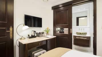 A hotel room with a bed, a desk with a lamp, a television, a mirror, and a minibar.