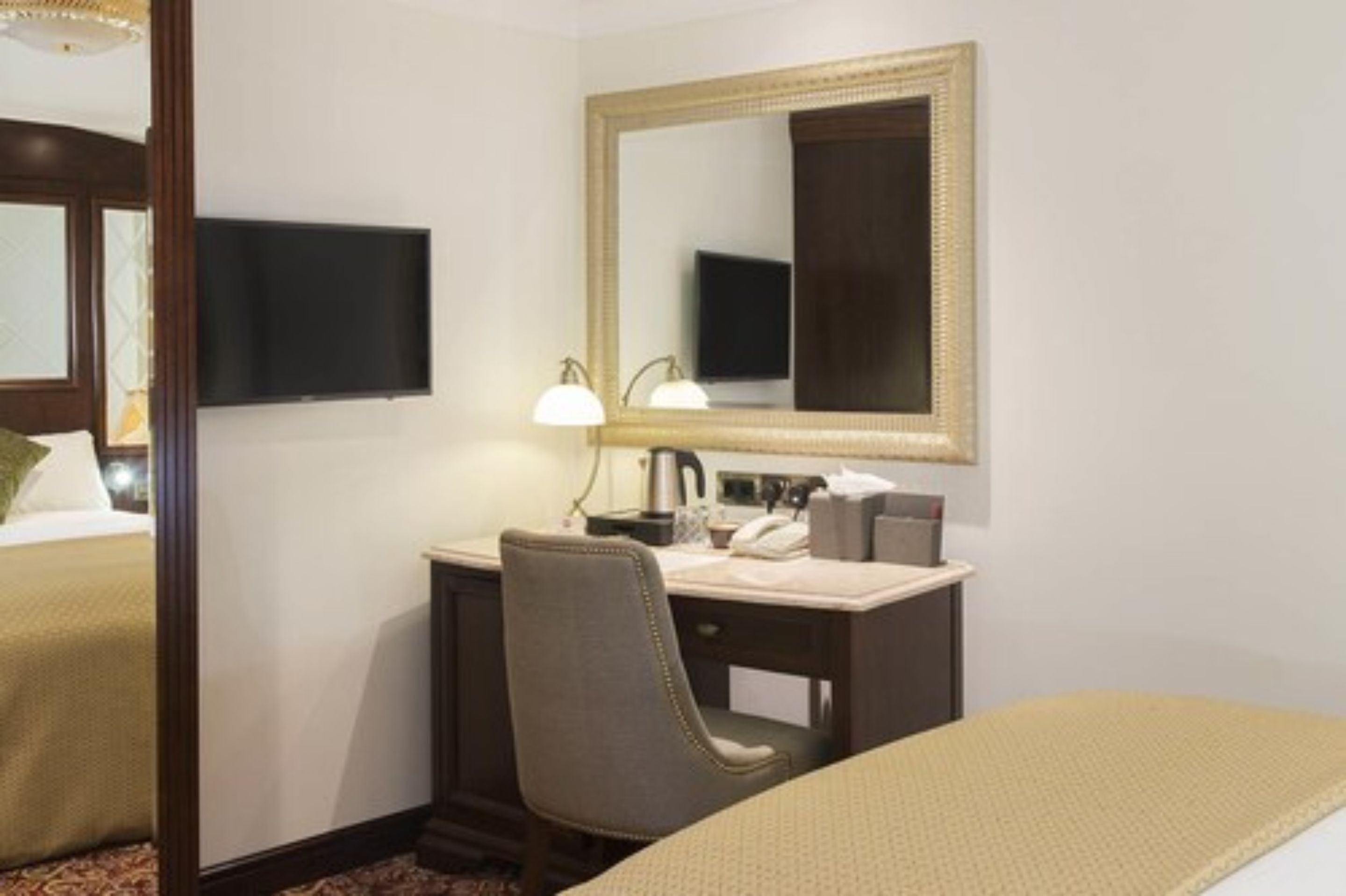 Una habitación de hotel con cama, escritorio, silla, espejo, televisor y lámpara.
