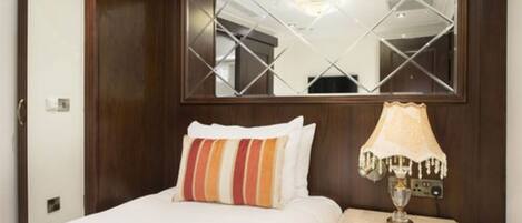 A hotel room with a bed, a nightstand, a lamp, and a large mirror.