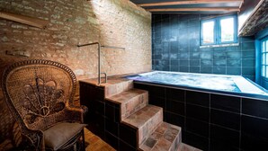 Un baño con paredes de piedra, una silla de madera, una bañera y una ventana.