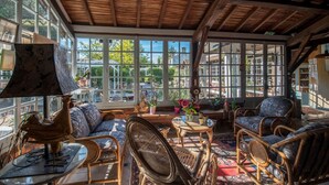 Una habitación iluminada por el sol con muebles de mimbre, ventanas amplias y vistas al exterior.