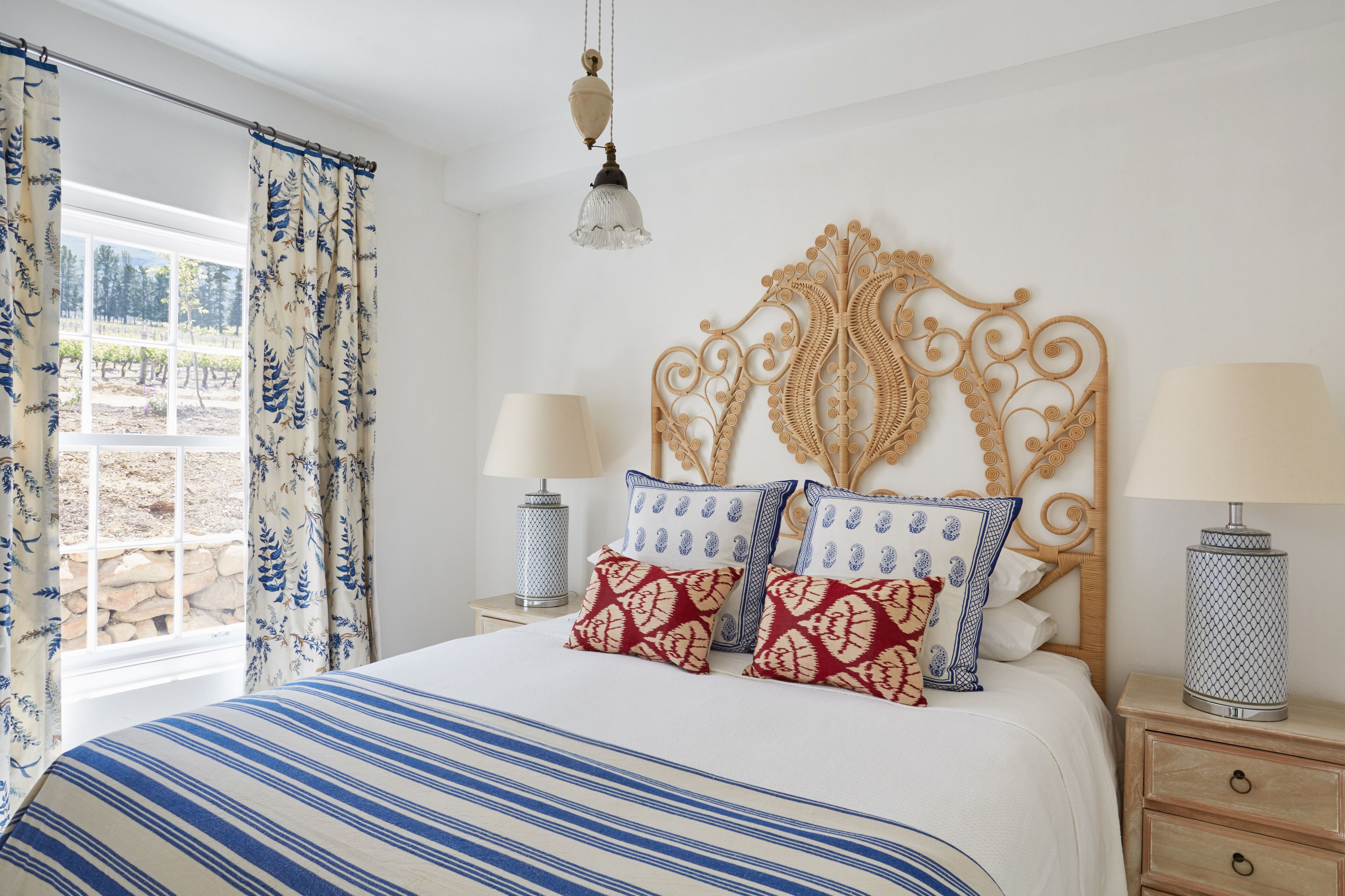 A bedroom with a bed, curtains, a headboard, bedside lamps, and a view of an outdoor area.