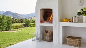 A stone-built outdoor oven with a fire, surrounded by wicker baskets and a metal rack.