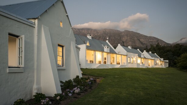 A row of white buildings with a sloped roof, set against a mountainous backdrop.