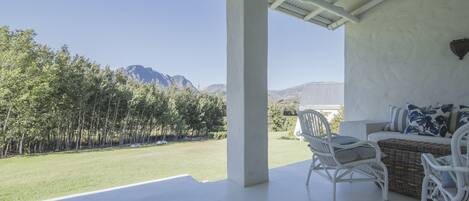 A covered patio with white wicker furniture, a view of a grassy area and mountains in the background.