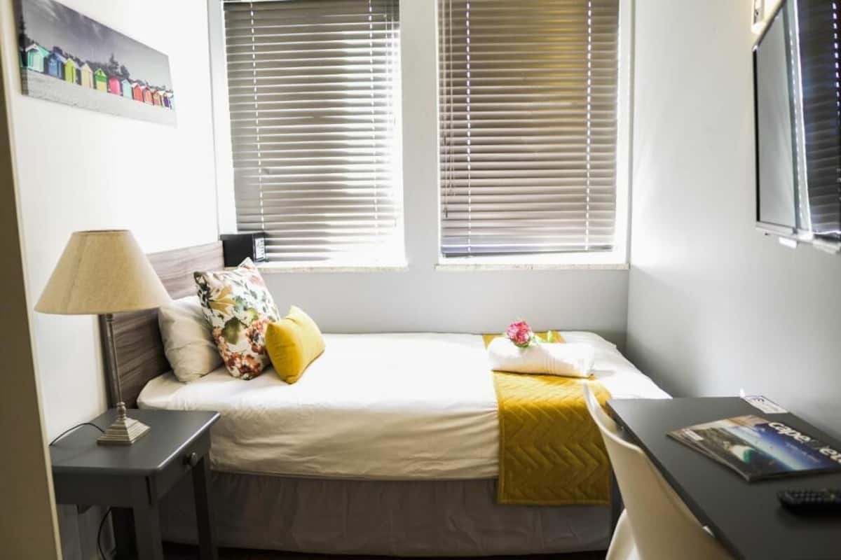 Une chambre à coucher avec un lit, une table de chevet, une lampe et une fenêtre avec des stores.