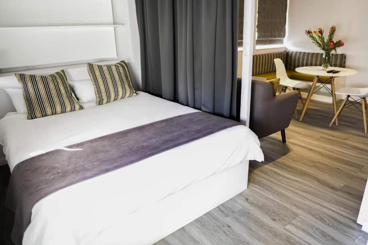 Une chambre d’hôtel avec un lit, un canapé, une table à manger et un vase de fleurs.