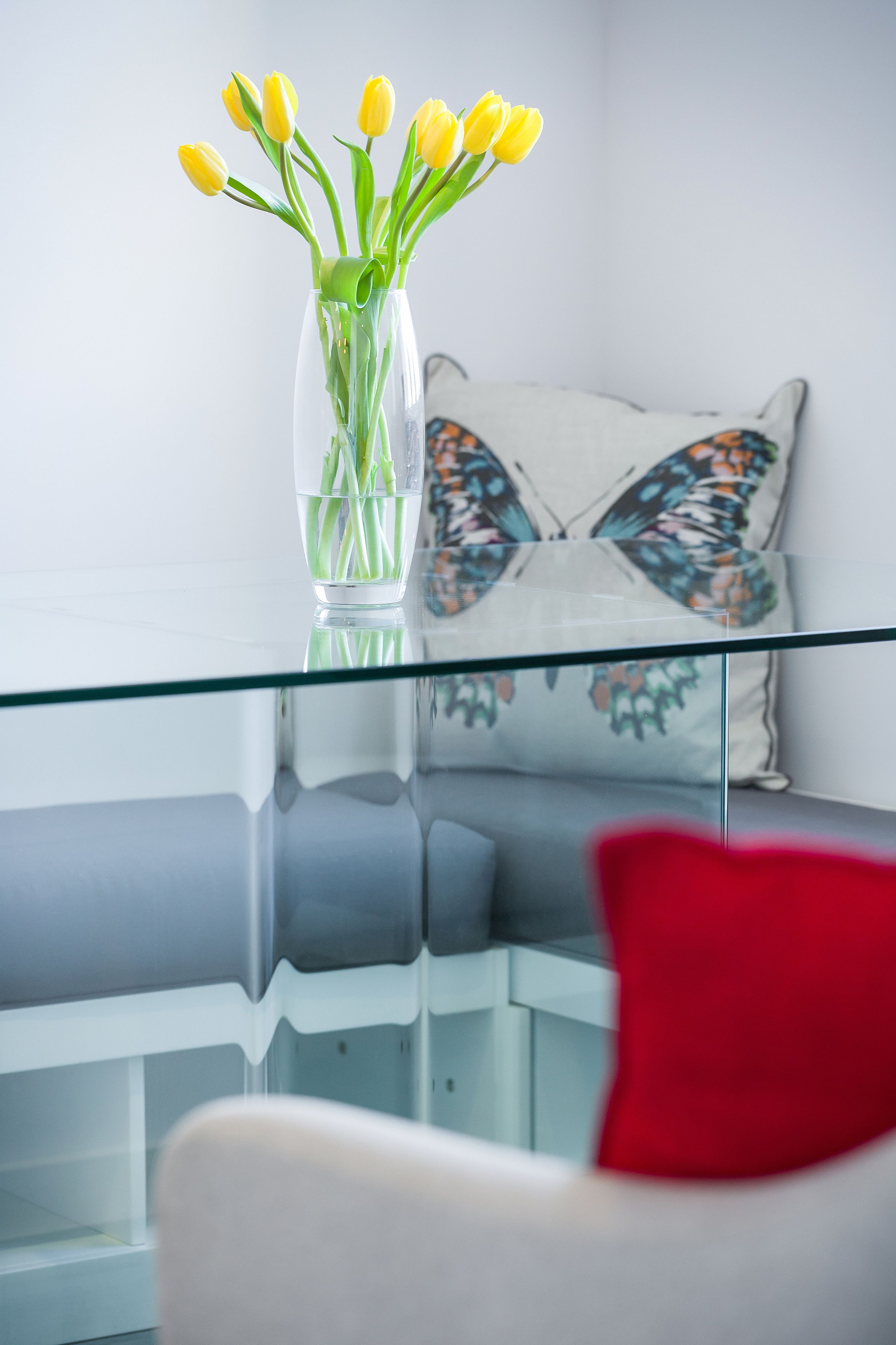 A clear glass vase with yellow tulips on a glass table.