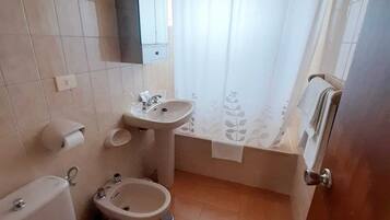 A compact bathroom with a toilet, bidet, sink, and bathtub.