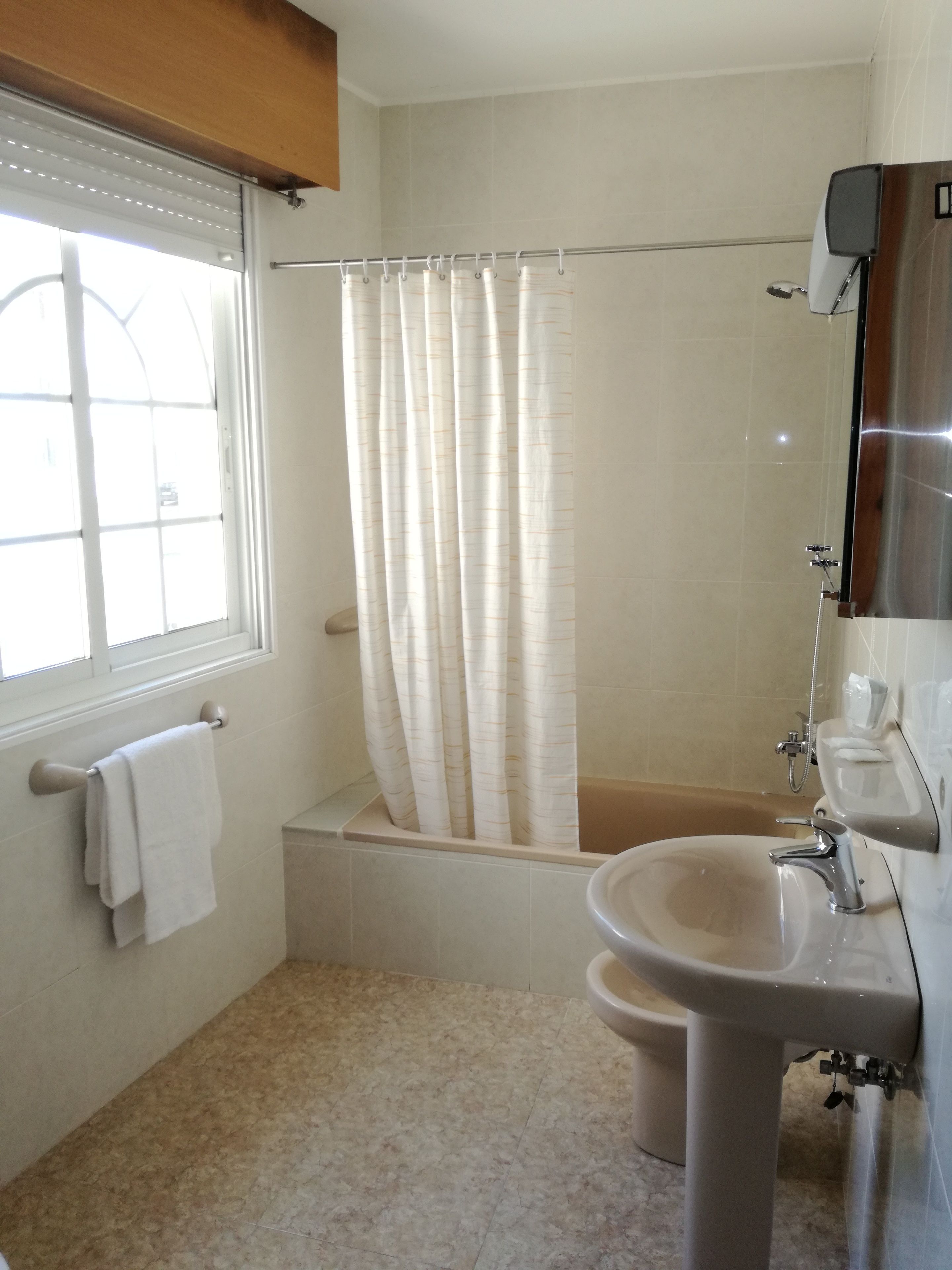 A bathroom with a bathtub, a sink, and a window with blinds.