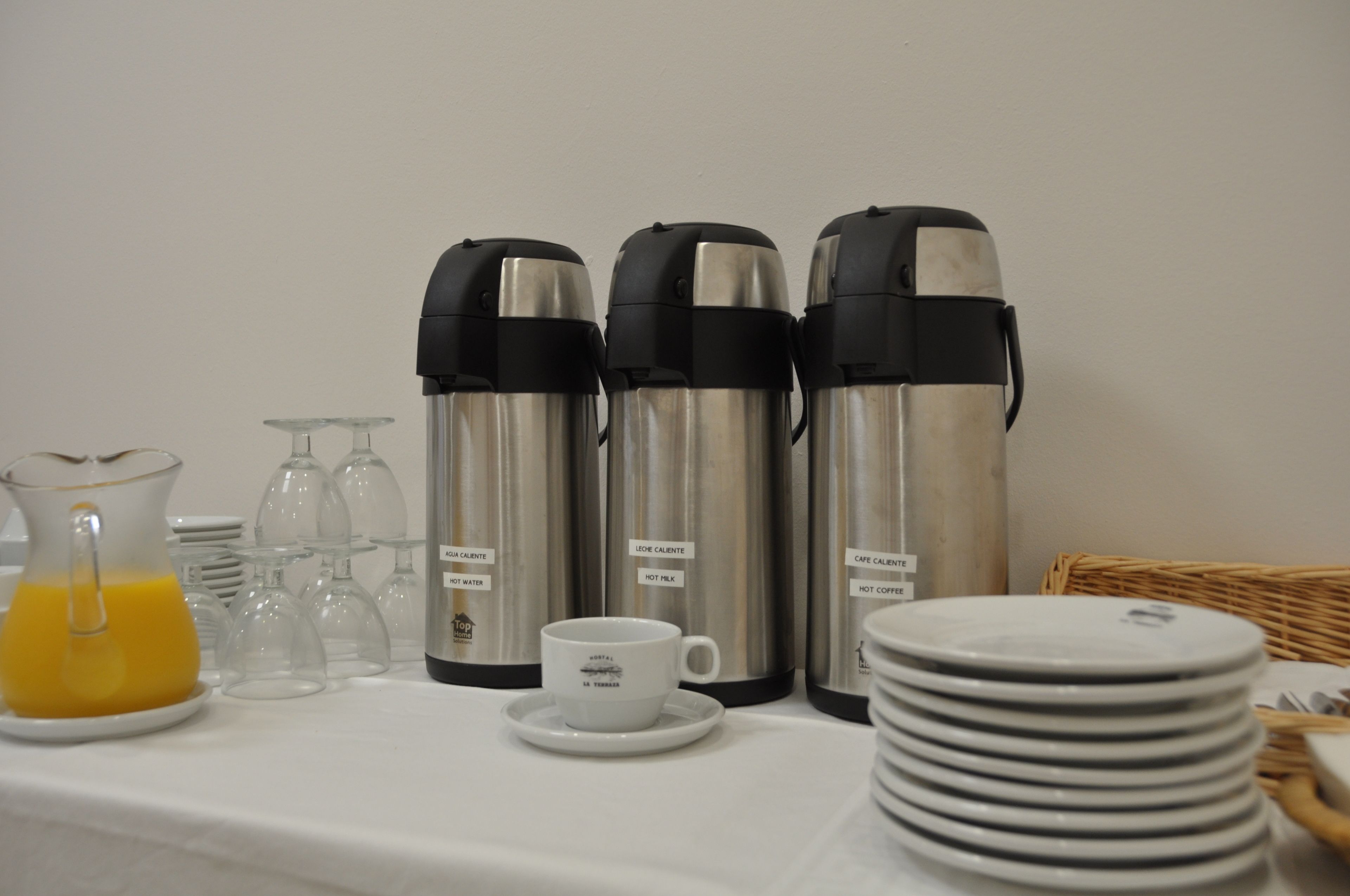 Una preparación para el desayuno con almohadillas calientes, una jarra de jugo de naranja y una taza sobre una mesa.