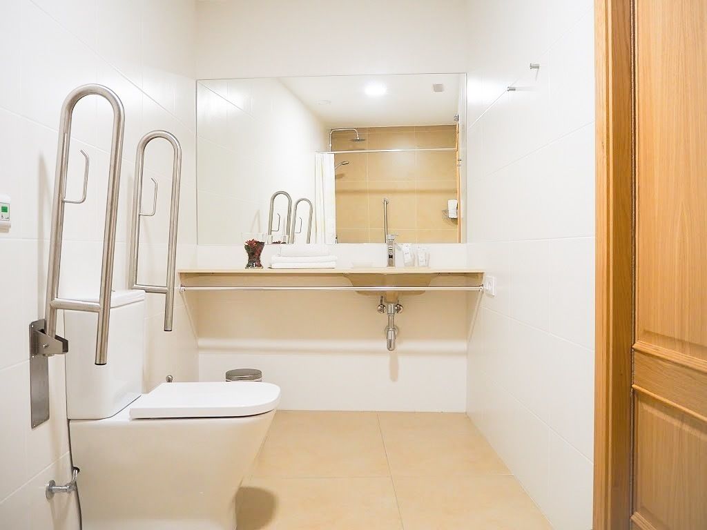 Une petite salle de bain moderne, équipée de toilettes, d’un lavabo et d’une douche. Un miroir est placé au-dessus du lavabo et une porte en bois se trouve sur le côté droit.