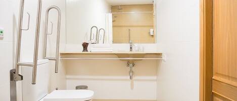 Un baño pequeño y moderno con inodoro, lavabo y ducha. Tiene un espejo sobre el lavabo y una puerta de madera a la derecha.