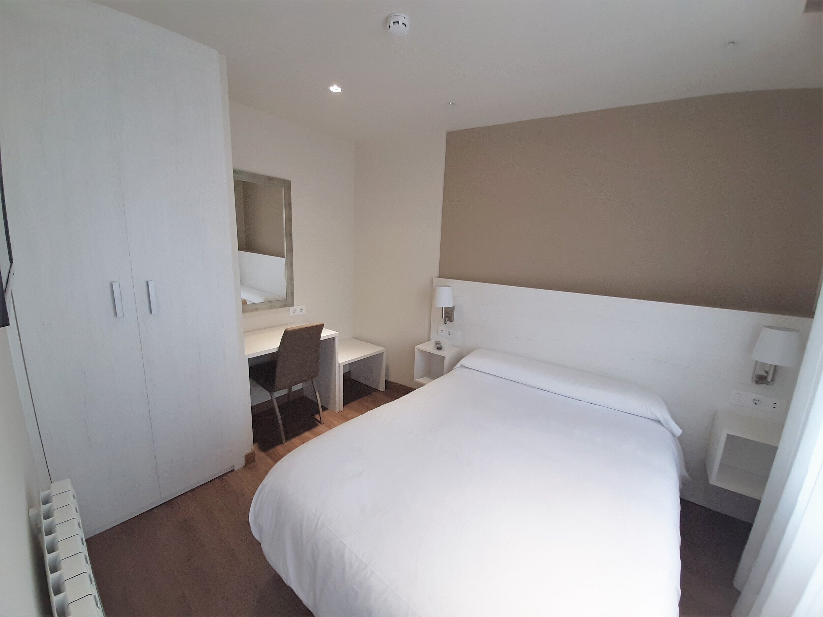 Une chambre d’hôtel comprenant un lit, un bureau, une chaise, une armoire et un miroir.