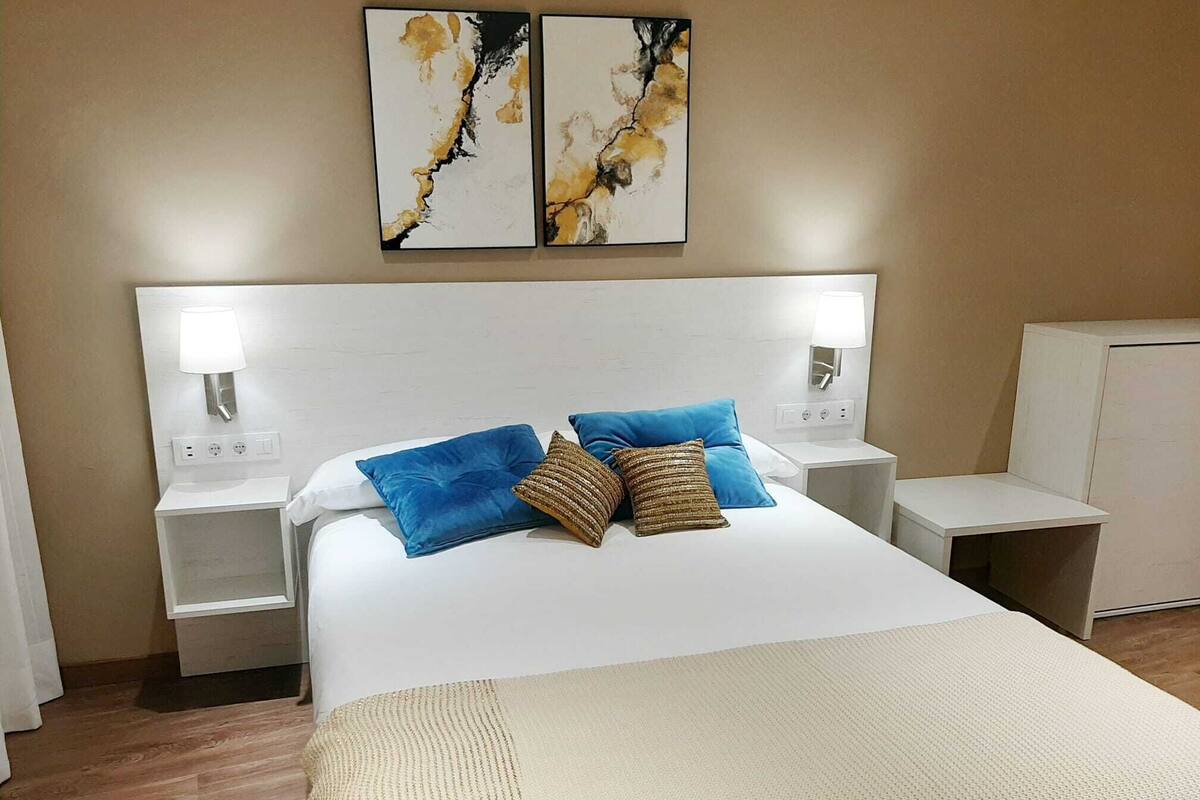 Ein Hotelzimmer mit einem großen Bett, zwei Wandleuchten und zwei abstrakten Bildern über dem Bett.