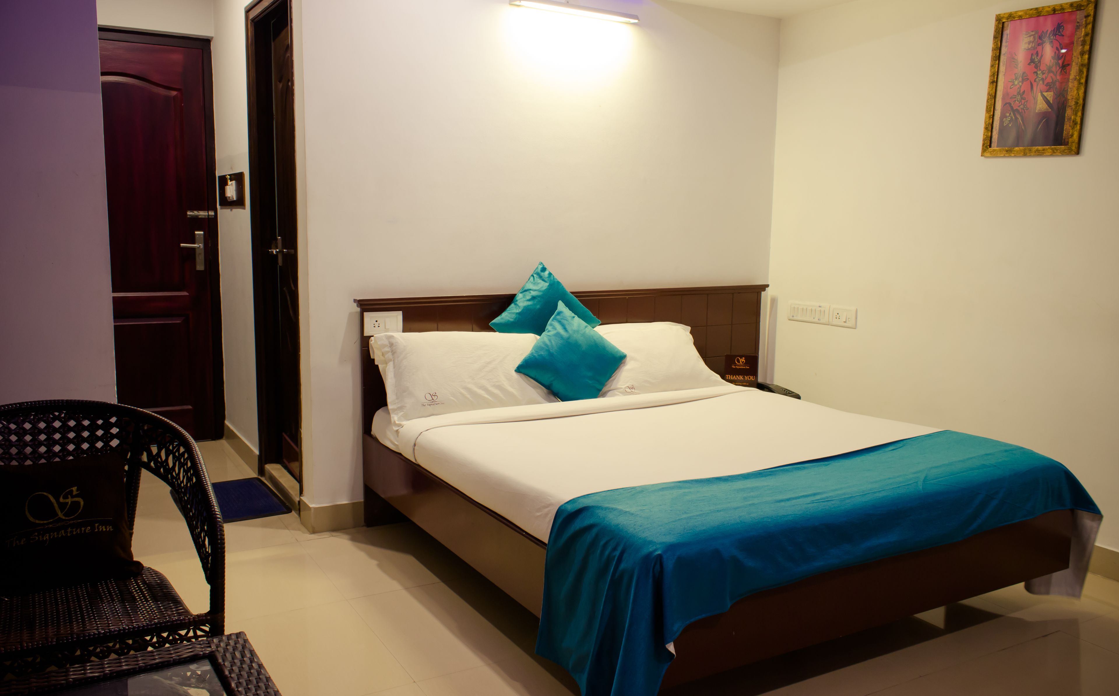 Una cama bien hecha con sábanas blancas, dos almohadas color turquesa, un cabecero de madera y una colcha azul.