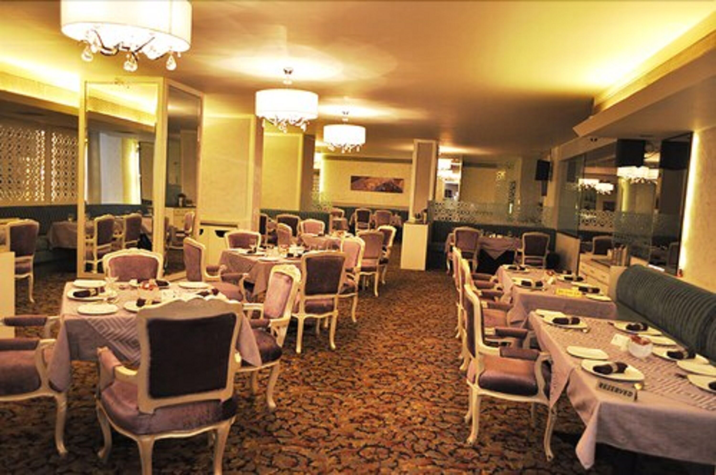 A hotel dining area with multiple tables and chairs, chandeliers, and a patterned carpet.
