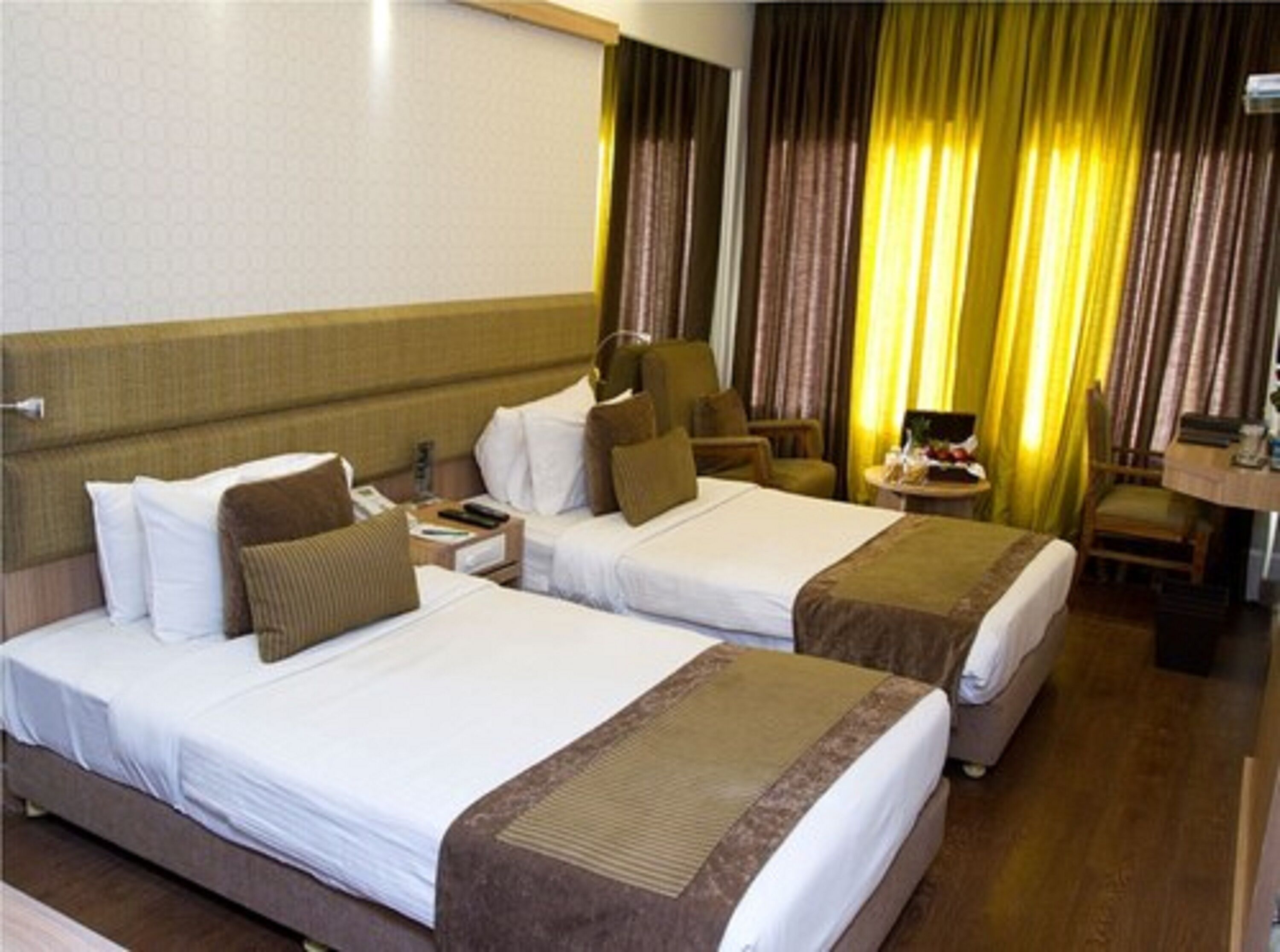 Ein Hotelzimmer mit zwei Betten, einem Schreibtisch, einem Stuhl und Vorhängen.