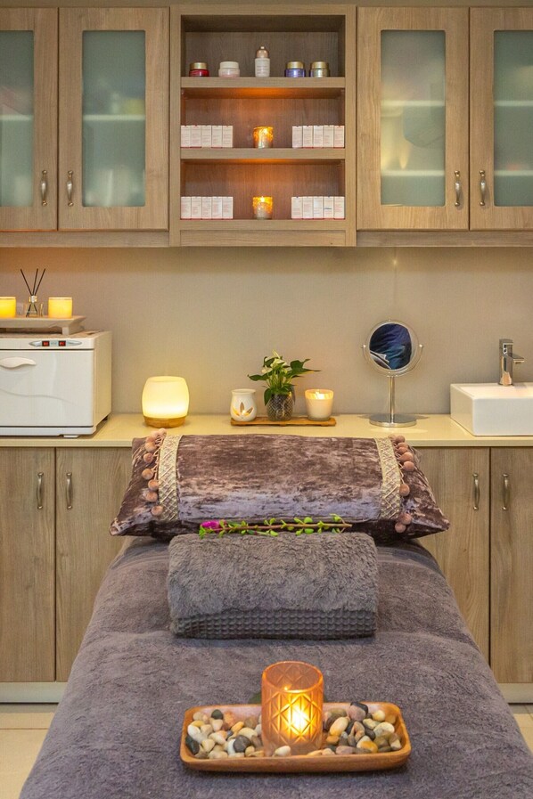 A spa room with a massage table, candles, a diffuser, and a shelf with spa products. - La Plume Boutique Hotel & Spa (Oudtshoorn)