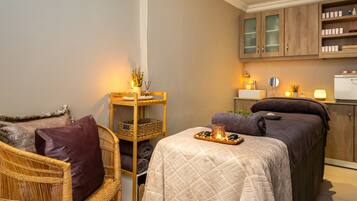 Una habitación acogedora con una cama, un sillón de mimbre, una mesita con velas y un armario con artículos de aseo.