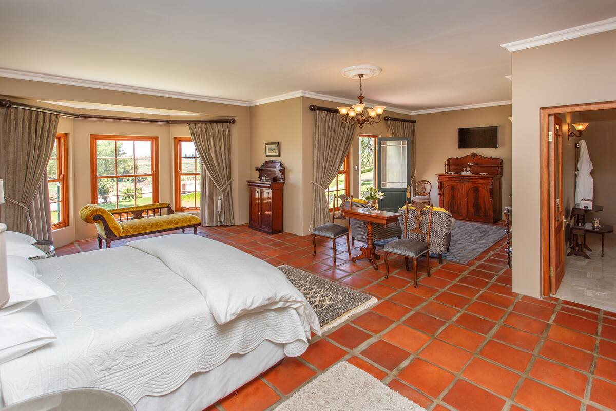 A spacious bedroom with a large bed, a sitting area with a bench, a desk, and a chair.