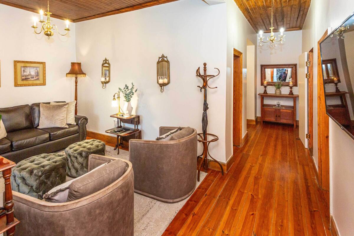 A cozy living room with a dark leather sofa, tufted ottomans, a wooden coffee table, and a chandelier.